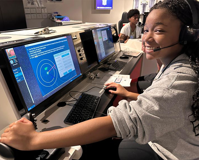 Female student sitting and a computer with head set on.