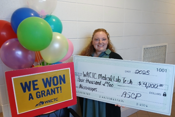 MLT Instructor holding a check in the amount of $4,000 from ASCP next to a sign 
